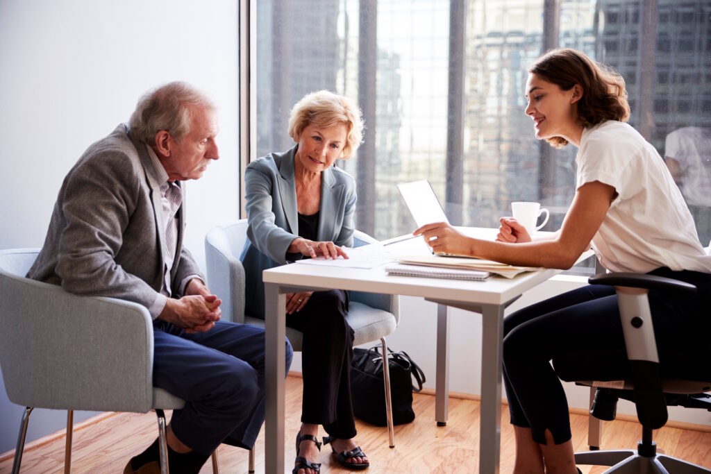 Three professionals sharing a discussion around a table with documents in a bright office.