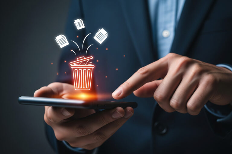Hands holding a smartphone with a glowing red trash can icon and flying paper documents, symbolizing deleting files on mobile.